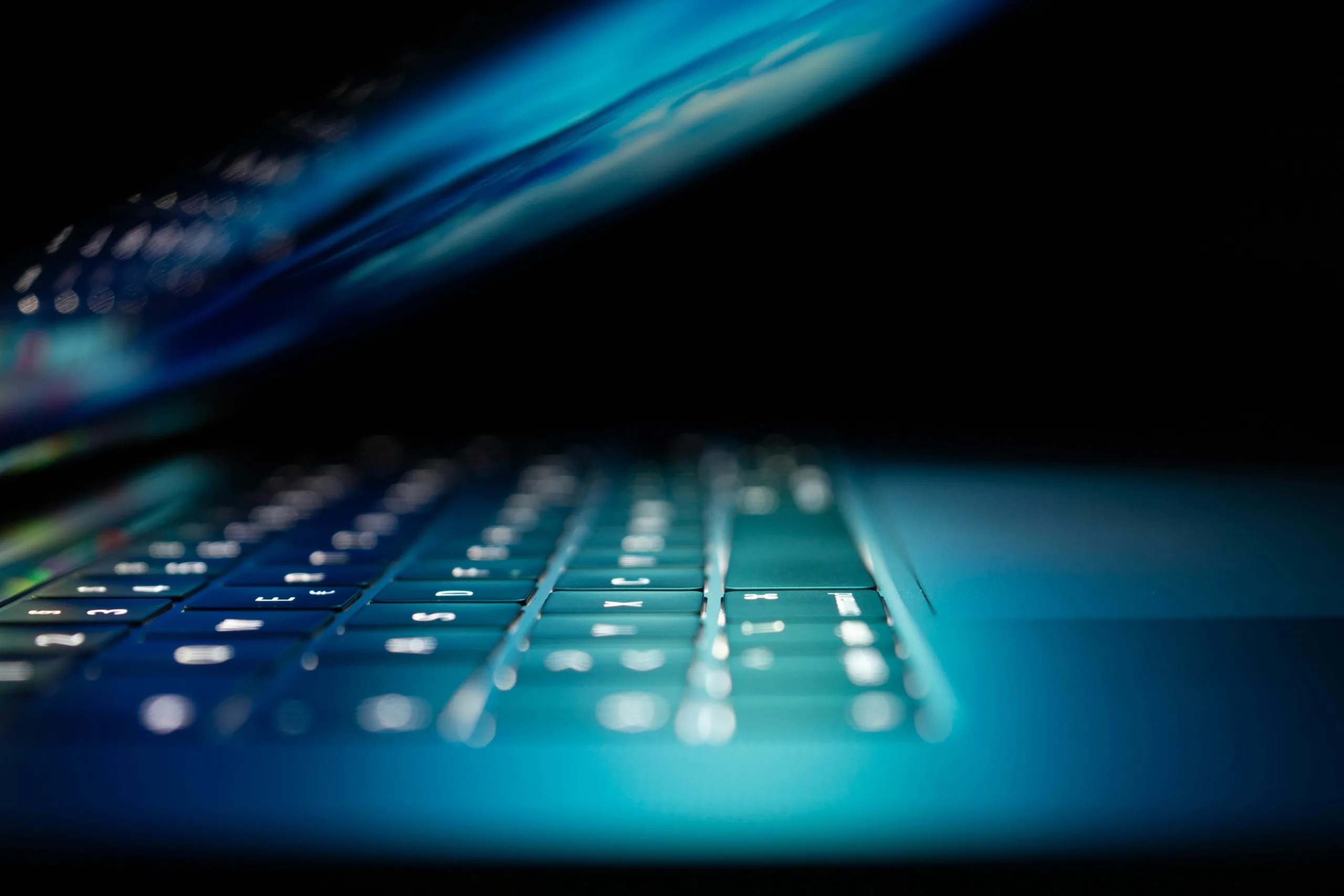 Image d'un laptop allumé et à moitié refermé dans une ambiance sombre